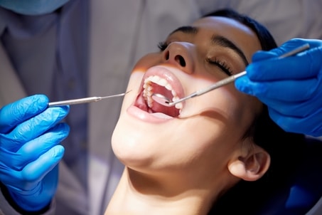 Close-up of dentist using tools to examine woman’s mouth during oral hygiene checkup and dental care appointment at clinic