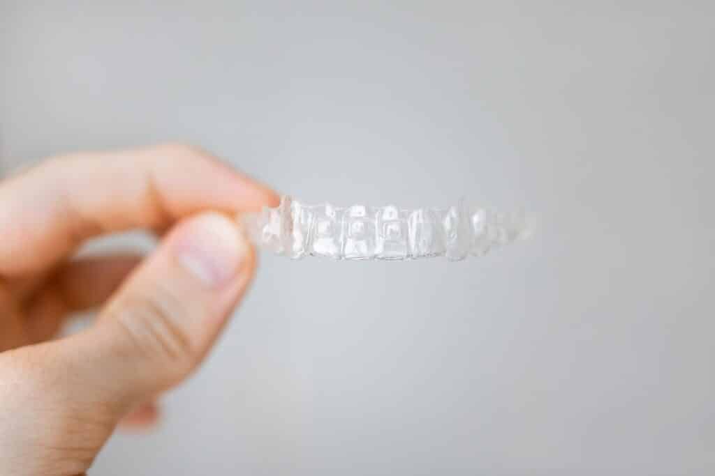 Close-up of clear dental aligner held in hand against neutral background, showcasing orthodontic solution for teeth straightening and dental care
