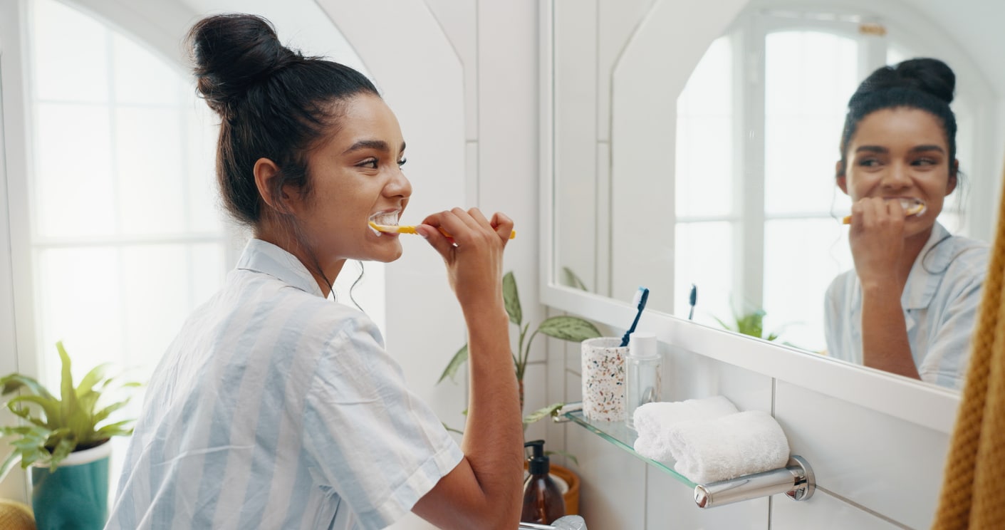 Woman brushing her teeth in front of a bathroom mirror as part of her daily oral hygiene routine.